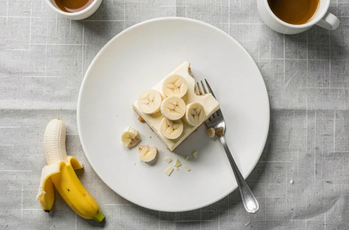 Vue de dessus d'une part de moelleux banane chocolat blanc sur une assiette blanche avec des copeaux de chocolat et une fourchette